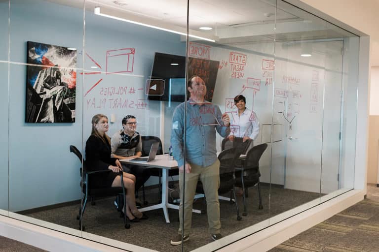 employees collaborating in meeting room writing on glass wall